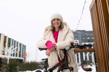 Bir kadın karda bir bisikletin yanında duruyor. O kış giysileri giyiyor ve bisiklet kar taneleriyle kaplı..