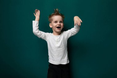 Genç bir çocuk canlı yeşil bir duvarın önünde tek başına duruyor. Yüzünde tarafsız bir ifadeyle dosdoğru karşıya bakıyor gibi görünüyor..