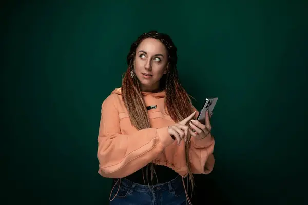 stock image A woman with dreadlocks is shown holding a cell phone in her hand. She appears to be using the phone and looking at the screen. Her hair is styled in thick, rope-like dreadlocks. The background is
