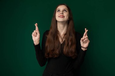 Katı yeşil bir duvarın önünde dik duran bir kadın doğrudan izleyiciye bakıyor. Tarafsız bir ifadeyle kendinden emin ve dengeli görünüyor. Arka plan yeşilin tek renk tonu.