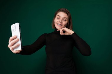 Bir kadın dışarıda cep telefonunu kol mesafesinde tutuyor ve selfie çekerken gülümsüyor..