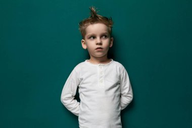 Canlı yeşil bir duvarın önünde duran genç bir çocuk resmediliyor. Önüne bakarken meraklı ve meşgul görünüyor..