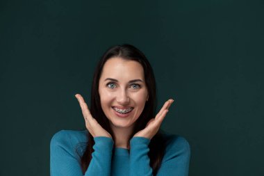 Bir kadın görüntüde, yüzünü komik bir şekle sokarken ellerini kullanarak yüzünü büker. İfadesi şakacı ve abartılı, fotoğrafta komik bir an yakalamış..