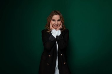 Bir kadın poz veriyor, ellerini yüzünü kapatıyor sanki fotoğraf için çerçeveliyormuş gibi. Kameraya poz verirken kendinden emin ve şık görünüyor. Arka plan basit.