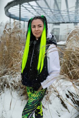 A woman with vibrant green hair stands in a snowy landscape, the cold white snow contrasting with her colorful hair. She looks around, her breath visible in the chilly winter air. clipart