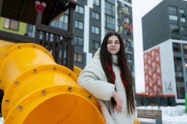 Bir kadın kocaman sarı bir yapının yanında duruyor ve ona tuhaf bir ifadeyle bakıyor. Nesne, boyutunu ve canlı rengini sergileyerek sahneyi domine ediyor gibi görünüyor..