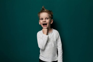 Sıradan giyinmiş genç bir çocuk parlak yeşil bir duvarın önünde duruyor, tarafsız bir ifadeyle ileriye bakıyor. Duvar, sahnedeki çocukların varlığına basit bir zemin görevi görüyor..