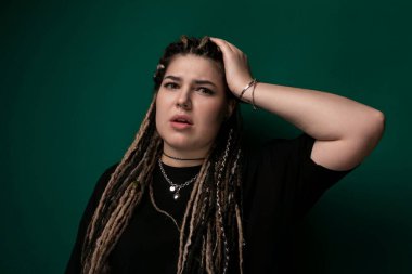 Rastalı bir kadın fotoğraf için poz veriyor, kameraya bakıyor. Saçları kalın, halat gibi sırtına kadar inen rastalar gibi, yüzünü çerçeveliyor. Ayağa kalktı.