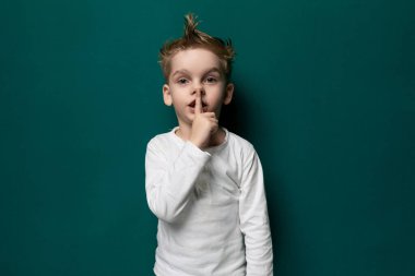 Genç bir çocuk canlı yeşil bir duvarın önünde duruyor, dümdüz ileriye bakıyor. Odaklanmış ve meraklı görünüyor, elleri yanı başında. Küçük figürle kalın duvar arasındaki zıtlık.