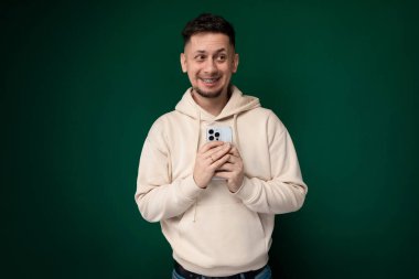 Adamın biri selfie çekmek için cep telefonunu tutuyor. Doğrudan telefon ekranına bakıyor ve gülümsüyor. Arka plan bulanık, adam ve telefonuna odaklanmış..