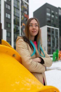 Bir kadın, beyaz manzarayla çelişen parlak sarı bir nesnenin yanında karın üzerinde duruyor. Kış aylarında nesneyi gözlemliyor ya da onunla etkileşime geçiyor gibi görünüyor..