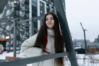 Karlı bir günde bir binanın önünde bir kadın duruyor. Binanın girişine doğru bakıyor gibi görünüyor, sıcak kış kıyafetleri içinde..