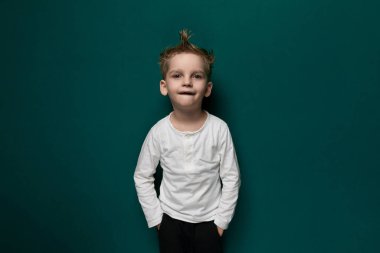 Pembe elbiseli genç bir kız, parlak yeşil bir duvarın önünde güvenle duruyor. Meraklı ve çevresiyle meşgul görünüyor, yüzünde hafif bir gülümsemeyle..