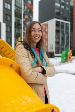 Bir kadın parlak sarı bir yapının önünde duruyor, düşünceli görünüyor. Sahne kentsel ve modern, kompozisyonun odak noktası kadın..