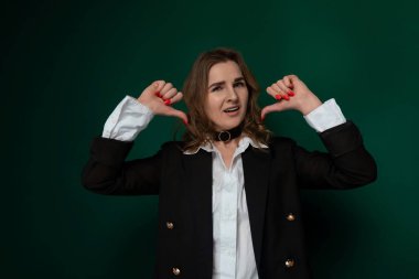 Siyah ceket giyen bir kadın, elleri başının arkasına sıkıca bağlanmış, kendinden emin bir şekilde durur. Rahatlamış ve sakin görünüyor. Kendine güveni tam gibi görünüyor..