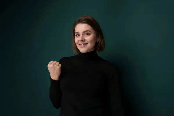 stock image A woman is standing upright in front of a vivid green wall. She appears to be gazing ahead, with a neutral expression on her face.