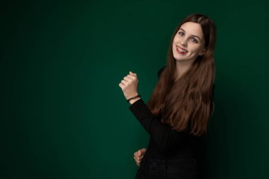 Parlak yeşil bir duvarın önünde duran bir kadın görülüyor. Direkt olarak kameraya tarafsız bir ifadeyle bakıyor. Duvar sade ve renklidir. Bu da bize arka planda kalmamızı sağlar.