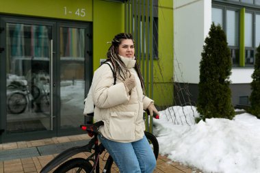 Kaldırıma park etmiş bir bisikletin yanında bir kadın duruyor. Gidona tutunurken uzaktaki bir şeye bakıyor gibi görünüyor..