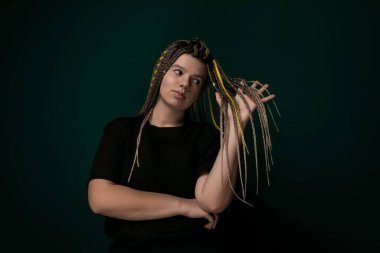 Rastalı bir kadın, kollarını kavuşturarak kendinden emin bir şekilde ayakta duruyor. Güçlü ve kendinden emin görünüyor. Güçlü ve kendine güvenen biri gibi görünüyor..