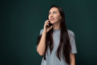 Dışarıda cep telefonuyla konuşan bir kadın var. Konuşurken telefonu kulağına dayıyor. Arka planda binaları ve arabaları olan bir şehir caddesi var..