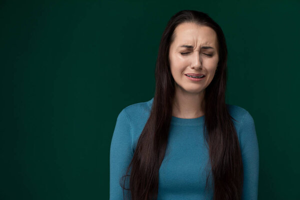 A woman stands in front of a bright green background with her eyes closed. She appears relaxed and focused, perhaps enjoying a moment of stillness and introspection.