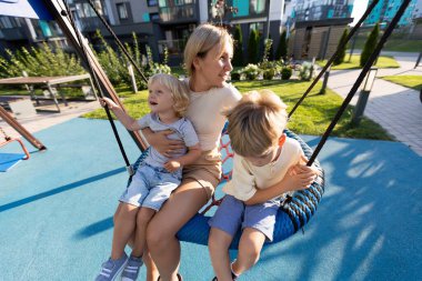 Bir anne, oyun parkında sallanırken iki oğluyla keyifli anlar paylaşır. Çocuklar, modern binalar ve yeşil alanlarla çevrili oyun zamanlarını gülüp eğlenerek geçiriyorlar. Çok güzel.
