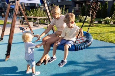 Bir anne, canlı bir oyun parkında birlikte oynayan iki oğluyla meşgul olur. Oğullardan biri salıncakta sallanırken diğeri yanında durup annesine ulaşmaya çalışıyor. Sahne güneşli bir havada geçiyor.