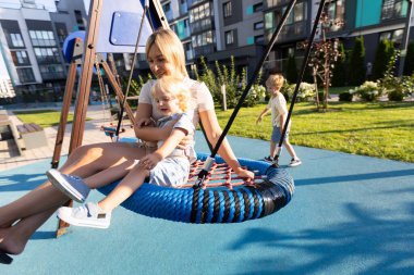 Bir anne renkli bir çocuk parkında iki oğluyla meşgul. Oğullardan biri salıncakta sallanırken, diğer oğlu yakınlarda oynarken, o anın tadını çıkarıyor. Parlak öğleden sonra güneşi neşe saçar