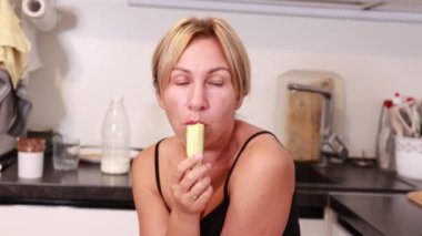 Bir kadın mutfağında oturmuş, taze bir şeyler atıştırıyor. Mutfağın sıcak atmosferi, tadını çıkarırken keyfine bakmasını sağlıyor..