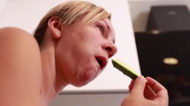 Beyaz bir kadın şık bir mutfakta lezzetli bir salatalığın tadını çıkarırken görülüyor. Basit bir yemek yeme, sağlıklı bir yaşam sürme zevkiyle meşgul. Sıcak atmosfer,