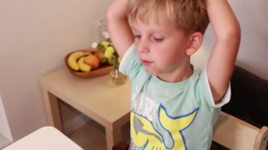 Genç beyaz bir çocuk mutfakta oturuyor, düşünceli bir şekilde aperatiflerine odaklanıyor. Yemeğin tadını çıkarırken meşgul ve meraklı görünüyor, çocukluk keşiflerinin tipik bir anını vurguluyor.