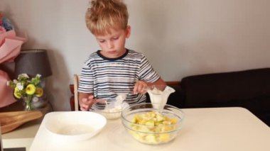 Genç beyaz bir çocuk aile mutfağında dikkatlice limonlu tatlı hazırlıyor. O, şeker ve taze malzemeleri karıştırmakla meşgul, yemek pişirme hevesini sergiliyor. Mutfak iyi aydınlatılmış.