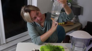 Açık renk saçlı bir kadın akvaryumunu geliştirmeye odaklanır. O, balığı için temiz bir çevre sağlarken dikkatlice akvaryuma su döker. Detaylara olan ilgisi bağlılığını vurguluyor.