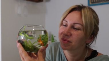 Kafkas bir kadın, canlı balıklarla dolu akvaryumuna dikkatle bakarken rahat bir şekilde oturur. Su yaşamının zarifçe yüzüşünü izlemekten zevk alıyor, düzeninin güzelliğini takdir ediyor. Şey...