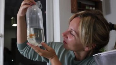 Bir kadın ev akvaryumuna su dolu bir torba ve canlı bir balık tutarak yeni bir balık sokmaya sevinçle hazırlanıyor. Yeni filmine hayran olduğu için hevesli ve meşgul görünüyor.