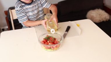 Neşeli bir Kafkasyalı çocuk aktif olarak yemek yapmakla ilgileniyor, bir kase taze salata malzemesine yağ ekliyor. Lezzetli bir yemek yaratma tecrübesinin tadını çıkarırken coşkusu içinden parlıyor.