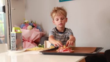 Genç bir çocuk aktif olarak mutfakta hevesle lezzetli bir yemek hazırlıyor. Aşçılığa olan sevgisini göstermek için malzemeleri tepsiye dikkatlice ekliyor. Konforlu mutfak seti ekliyor