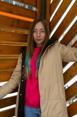 A woman standing upright in front of a wooden wall, looking straight ahead with a neutral expression. The wall behind her appears weathered and rustic, adding a textured backdrop to the scene. clipart