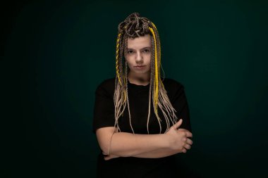 Parlak sarı rastalı bir kadın, kolları çapraz ama iddialı bir pozla, kendine güvenle duruyor, eşsiz saç stilini ve kendine güvenini sergiliyor..