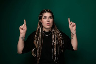 Rasta saçlı bir kadın kendinden emin bir şekilde kameraya bakıyor. Yüz ifadesi iddialı ve ilgi çekici. Sahnedeki varlığına dikkat çekiyor..