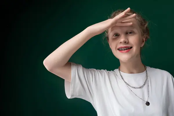 stock image A young woman is striking a pose for a photographer. She is standing confidently, adjusting her hair and smiling at the camera. The background is simple, allowing her to be the focus of the shot.