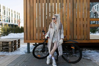 A woman standing next to a bicycle in a snowy landscape, wearing warm clothing. The bike is covered in snow, indicating it hasnt been used recently. clipart