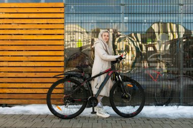 Bir binanın önünde bir kadın bir bisikletin yanında duruyor. Bisiklet yolculuğuna ara vermiş ya da ara vermiş gibi görünüyor. Arkasındaki bina modern ve geleneksel bir karışım.