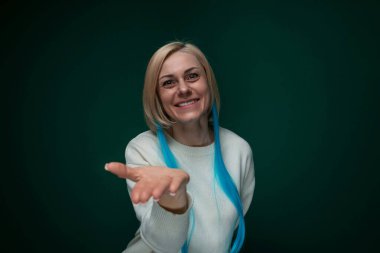 Bir kadın kameranın önünde duruyor, işaret parmağını doğrudan izleyiciye doğrultuyor yüzünde neşeli bir ifadeyle. İzleyiciyle iletişim kurarken kendinden emin ve arkadaş canlısı görünüyor..