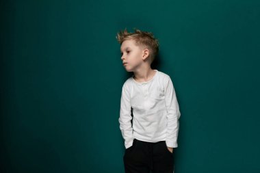 Genç bir erkek çocuk, katı yeşil bir duvarın önünde dikiliyor, dümdüz ileriye bakıyor. Duvar, çocukların orada bulunması için basit bir zıt zıtlık yaratıyor..