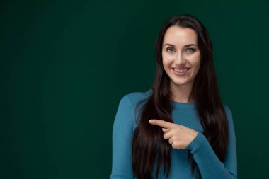 Bir kadın işaret parmağını, açıklanmayan bir nesneyi ya da yönü işaret etmek için kullanıyor. Hareketiyle dikkatleri üzerine çekiyor. Eli uzatılmış ve vücut dili hedefe odaklanmış görünüyor.