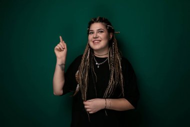 Çerçevenin dışındaki bir objeyi gösteren uzun saçlı bir kadın. Odaklanmış ve meşgul görünüyor, belli bir noktaya dikkat çekiyor. Hareketleri merakı veya vurguyu işaret ediyor..