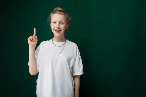 stock image A woman wearing a white t-shirt is pointing directly at the camera in a confident manner. The focus is on her action of pointing, while she stands against a neutral background.