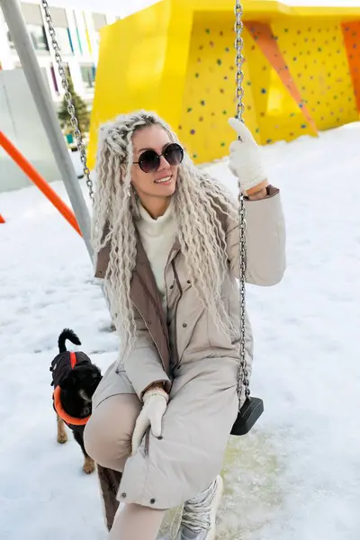 stock image A woman sits on a swing covered in snow, bundled up in warm clothing. The snow-covered ground contrasts with her dark outfit as she looks contemplative.