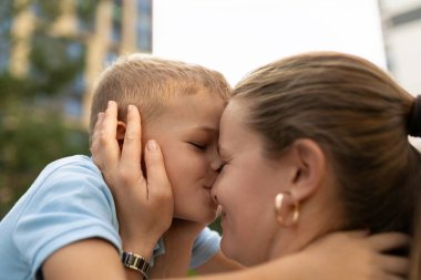 In a sunny park, a mother lovingly embraces her young son, sharing a sweet kiss and showcasing their warm relationship filled with joy and affection. clipart